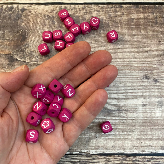 hand holding pink cube beads with letters